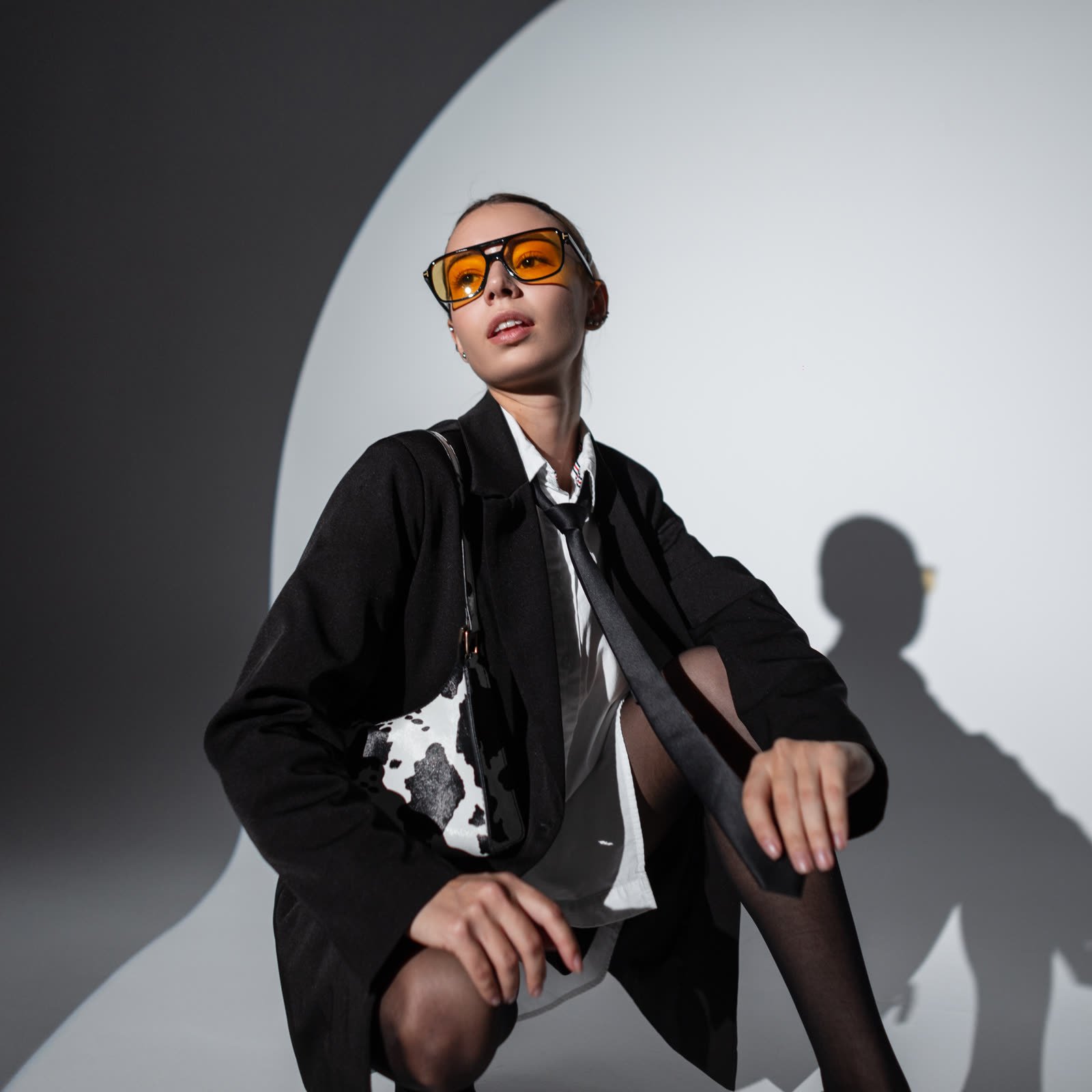 Woman in an oversized black blazer with sheer black tights and tinted glasses