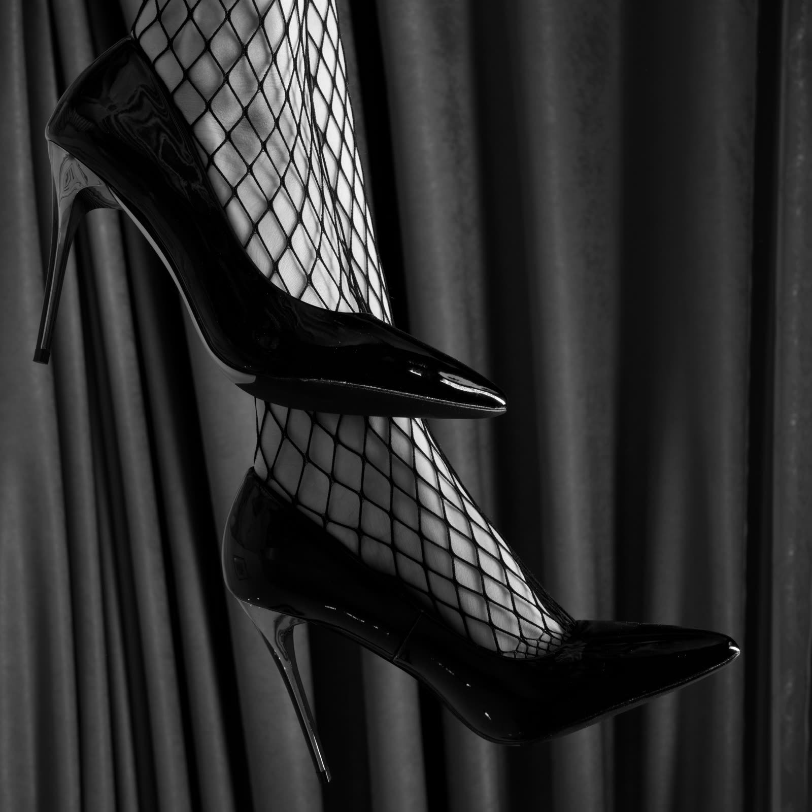 Black patent stiletto and fishnet stocking against a dark curtain