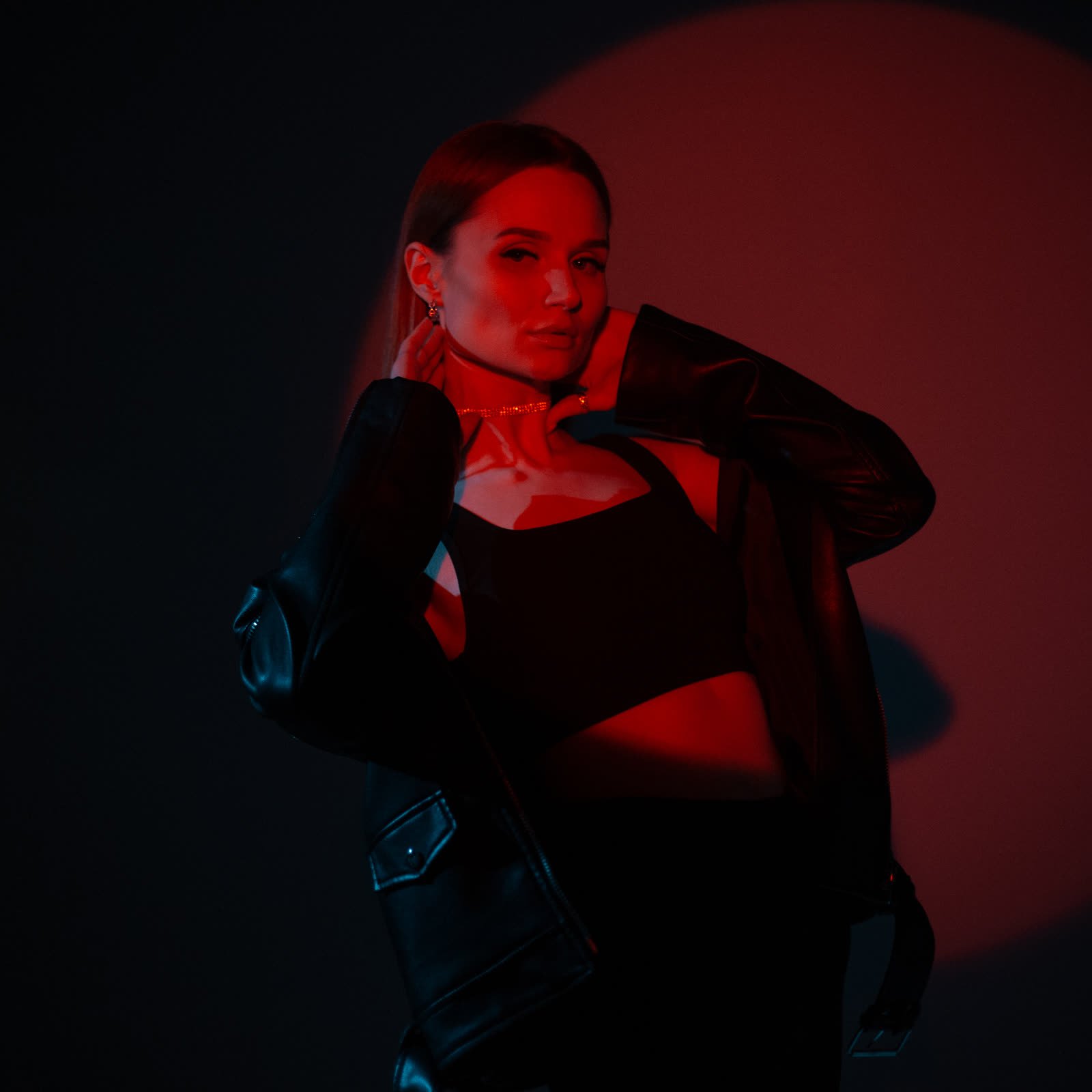 Woman in a black jacket over a cropped top in red and black light